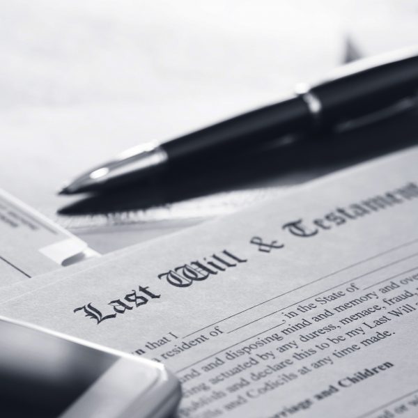 A ballpoint pen and a mobile phone rest on top of a last will and testament document that is part of the estate planning process.  This image is photographed using a very shallow depth of field.